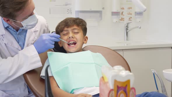 Young Boy Looking Scared, Having His Teeth Examined By Mature Dentist
