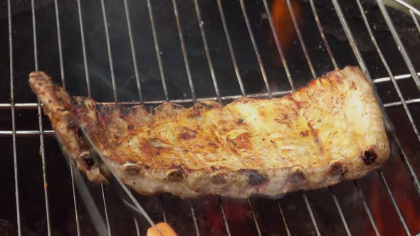 Delicious Ribs are Rotated on the Grill Grid on the Background of the Open Fire