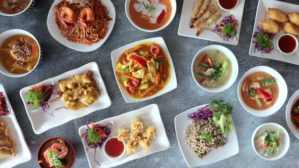 Male hand rotating small bowl of thai cuisine on flat lay table top.