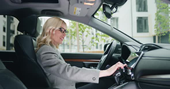 Female Mature Driver in Formal Clothes Adjusting Radio Dial Button Control, gps or Air Conditioning