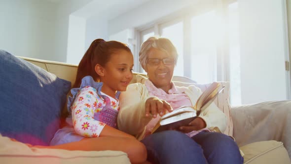 Grandmother and daughter reading book in living room 4k