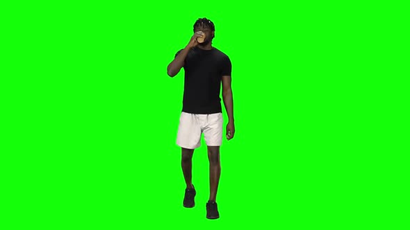 African American Man Walking and Drinking Coffee at Green Screen, Chroma Key. Front View. Slow