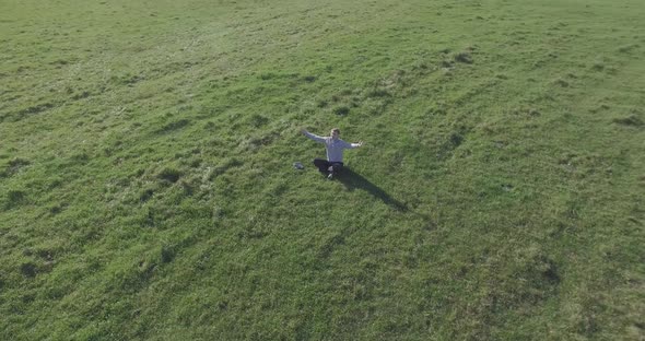 Low Orbital Flight Around Man on Green Grass with Notebook Pad at Yellow Rural Field.