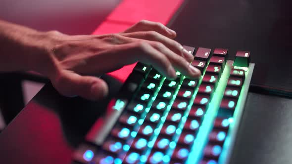 Young Gamer Plays a Video Game Closeup of Hands on the Keyboard Illuminated Coral Color and