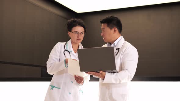 Asian Doctor and Female Physician Having Meeting in Medical Clinic Using Laptop