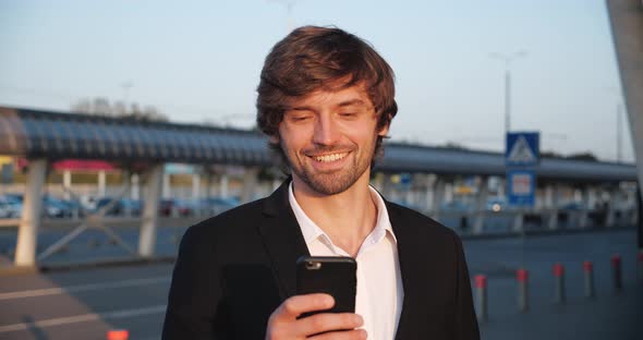 Portrait of Caucasian Successful Businessman is standing outdoor near the Parking full of Cars.