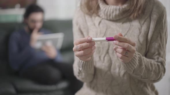 Close-up of Young Caucasian Woman Holding Pregnancy Test with Both Hands and Putting Them on Chest