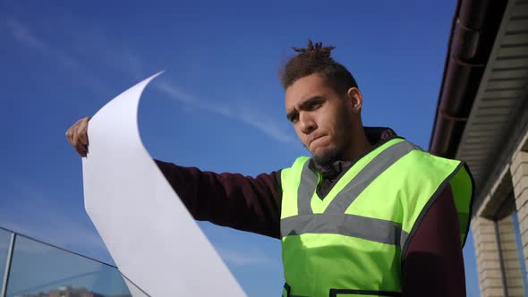 Bottom Angle View of Confident Positive Contractor Analyzing Building Blueprint Looking Away at