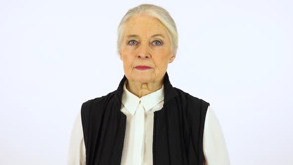 An elderly woman looks seriously at the camera - white screen studio