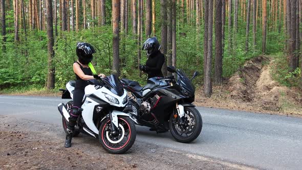 Motorbikes in the Forest  Two Women Steps Off Their Motorcycles and Takes Off Their Helmets
