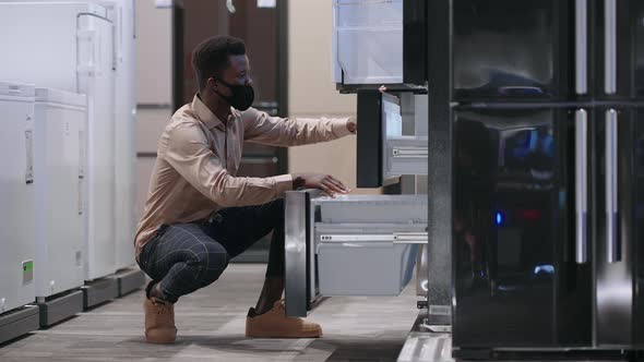 Afroamerican Guy is Choosing Fridge in Home Appliance Store Viewing Exhibition Sample Opening Doors