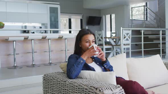 Mixed race woman sitting on couch drinking cup of coffee