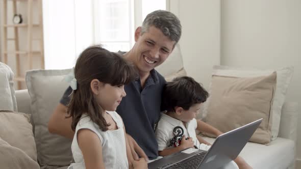 Cheerful Dad and Two Cute Kids Sitting at Laptop in Living Room