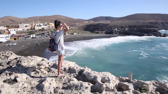 Beautiful young woman standing at the top of a cliff and watching the ocean