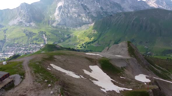 Drone shot of a Ski Resort in the summer with Mountains in the Background and Patches of Snow