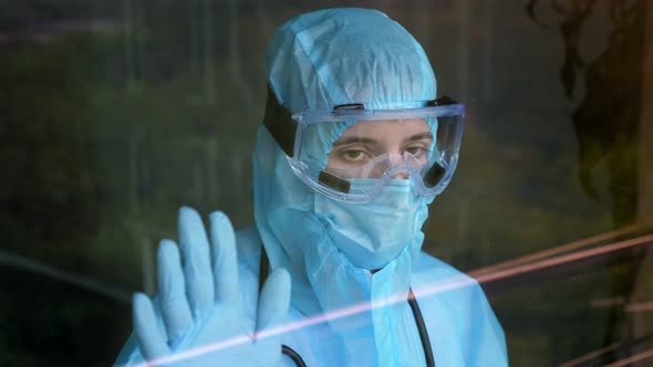 Medical Worker in Special Protective Suit. Tired and Exhausted Doctor Leaned Against the Window