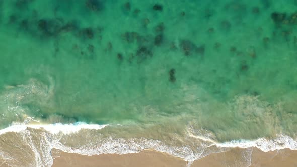 Crystal clear water and crashing waves onto the California coastline from an Ariel drone view.