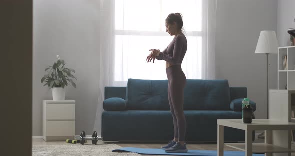 Sportswoman Is Training Alone in Living Room Viewing Smartwatch and Squatting with Jumps Home