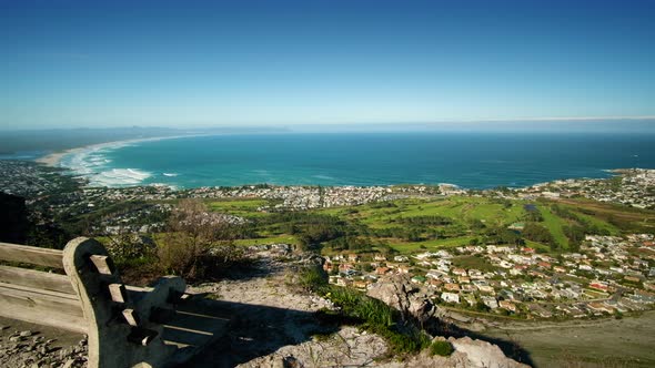 Panning shot from behind bench at scenic view point on mountain, overlooking bay and coastline of fi