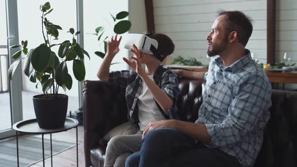 Father sitting on couch with son wearing virtual reality simulator