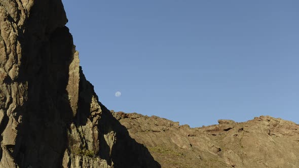 Time lapse of moon rising in sky behind mountains