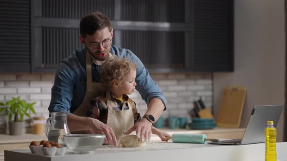 Young Father with His Little Son are Cooking Kneading Dough on Kitchen Table in Modern Apartment