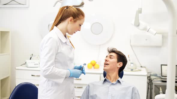 Young Friendly Female Dentist Talking with Male Patient Sitting in Chair About Oral Health Hygiene