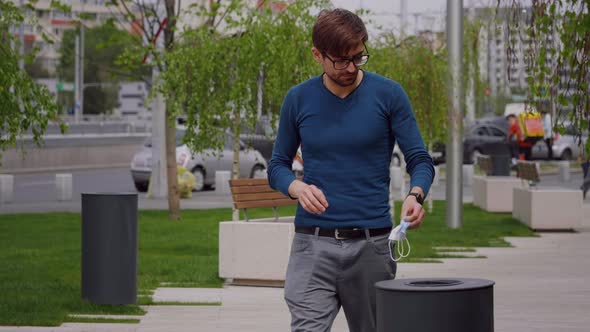 Young man walking around town take out the surgical mask and throw it in the trash.