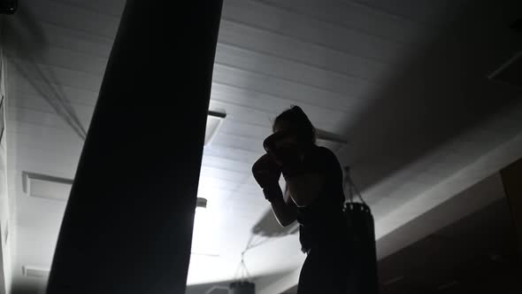 Dark Silhouette of a Boxer Girl Practicing Punches on a Boxing Bag