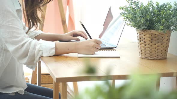 young smiling Asian woman working on laptop while at home in office work space.