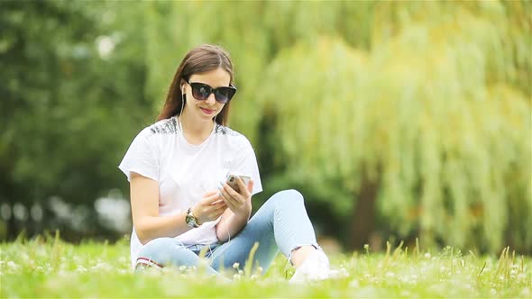 Cute Woman Is Reading Text Message on Mobile Phone While Sitting in the Park.