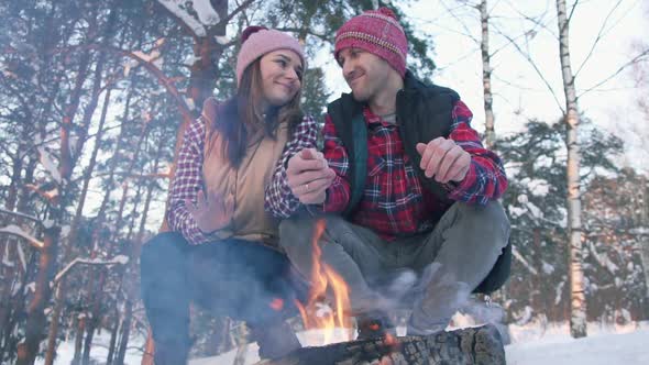 a Pair of Young People in Red Shirts in the Woods Warm Their Hands By the Fire a Winter Picnic