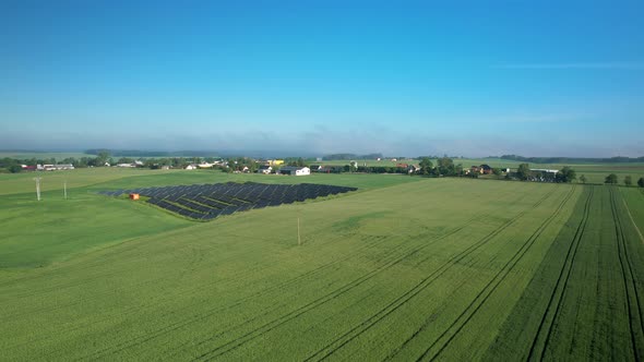 Aerial: Solar Panel Units and Wind Turbine on green grass field with blue sky