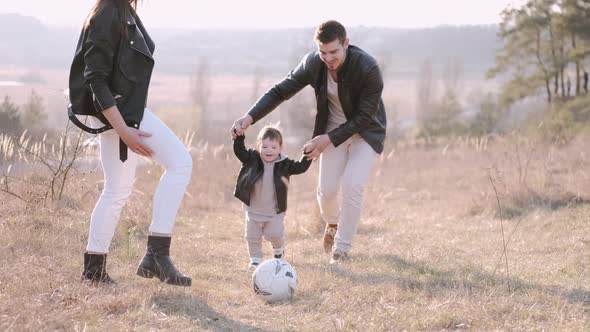 Happy Parents and a Cute Son Are Playing Football Outside