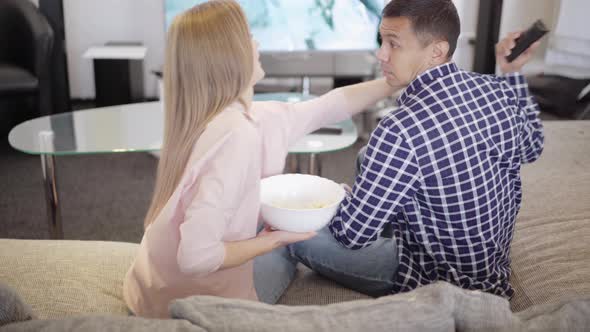 Back View of Carefree Young Caucasian Couple Having Fun Fighting for Popcorn and Remote Control at