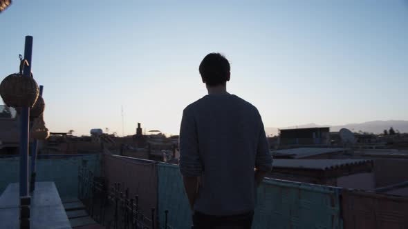 SLOW MOTION: YOUNG MAN WALKING ON ROOFTOP TERRACE WITH EARLY MORNING SUNRISE IN BEAUTIFUL BLUE AND