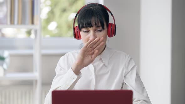 Young Beautiful Woman in Headphones Yawning and Typing on Laptop Keyboard