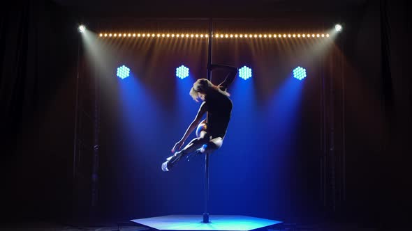 The Leggy Blonde Spins on a Pole with Her Arms Around Herself