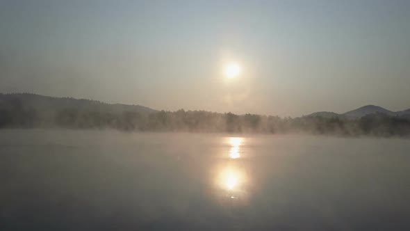 Cinematic Aerial Fly Through a Morning Fog Over a Mountain Lake. Foggy Sunrise In Mountains.
