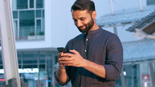 Smiling Indian Business Man Using Phone Texting Standing in Urban City Outside