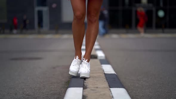 Women's Feet in White Highsoled Shoes Walk on a Very Narrow Sidewalk