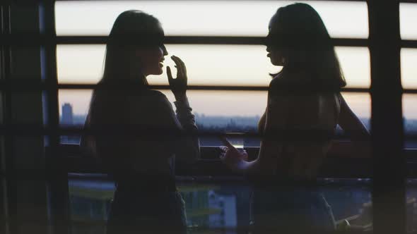 Two girls having drinks and talking on the balcony with a city view