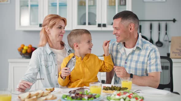 Parenting Adorable Male Child with Fish in Hands Sits in Woman Arms and Feeds His Happy Father While