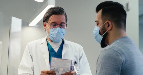 Mature Doctor in Mask Giving Prescription to Patient