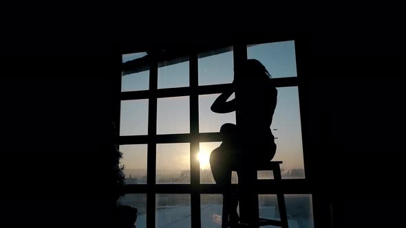 Silhouette of Lady Sitting and Dancing on Stool at Sunset