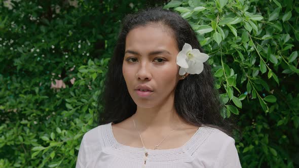 Portrait of a Young Beautiful Thai Woman with a Flower in Her Hair Standing in a Garden and Looking
