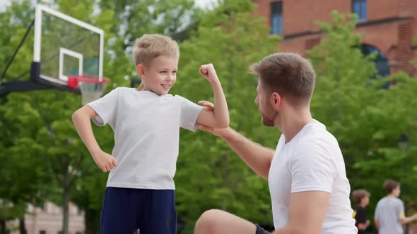 Father and Son Smiling and Showing Their Muscles Outdoors