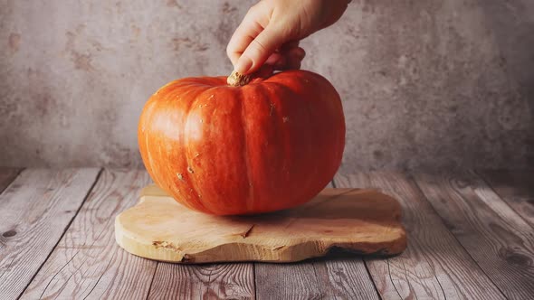 Female Hand Placing a Big Orange Pumpkin on Wooden Board