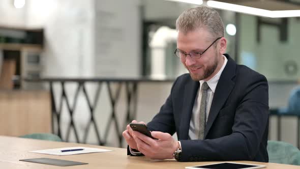 Young Businessman Celebrating Success on Smartphone in Office