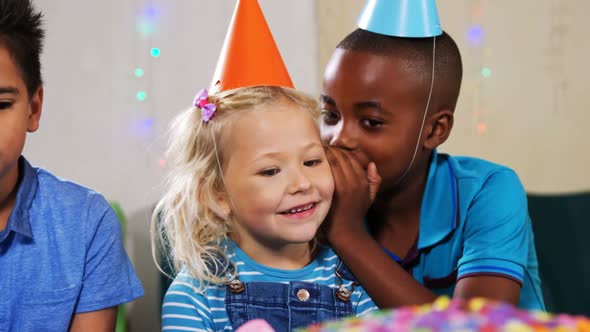 Boy whispering to girl while sitting with friends during birthday party